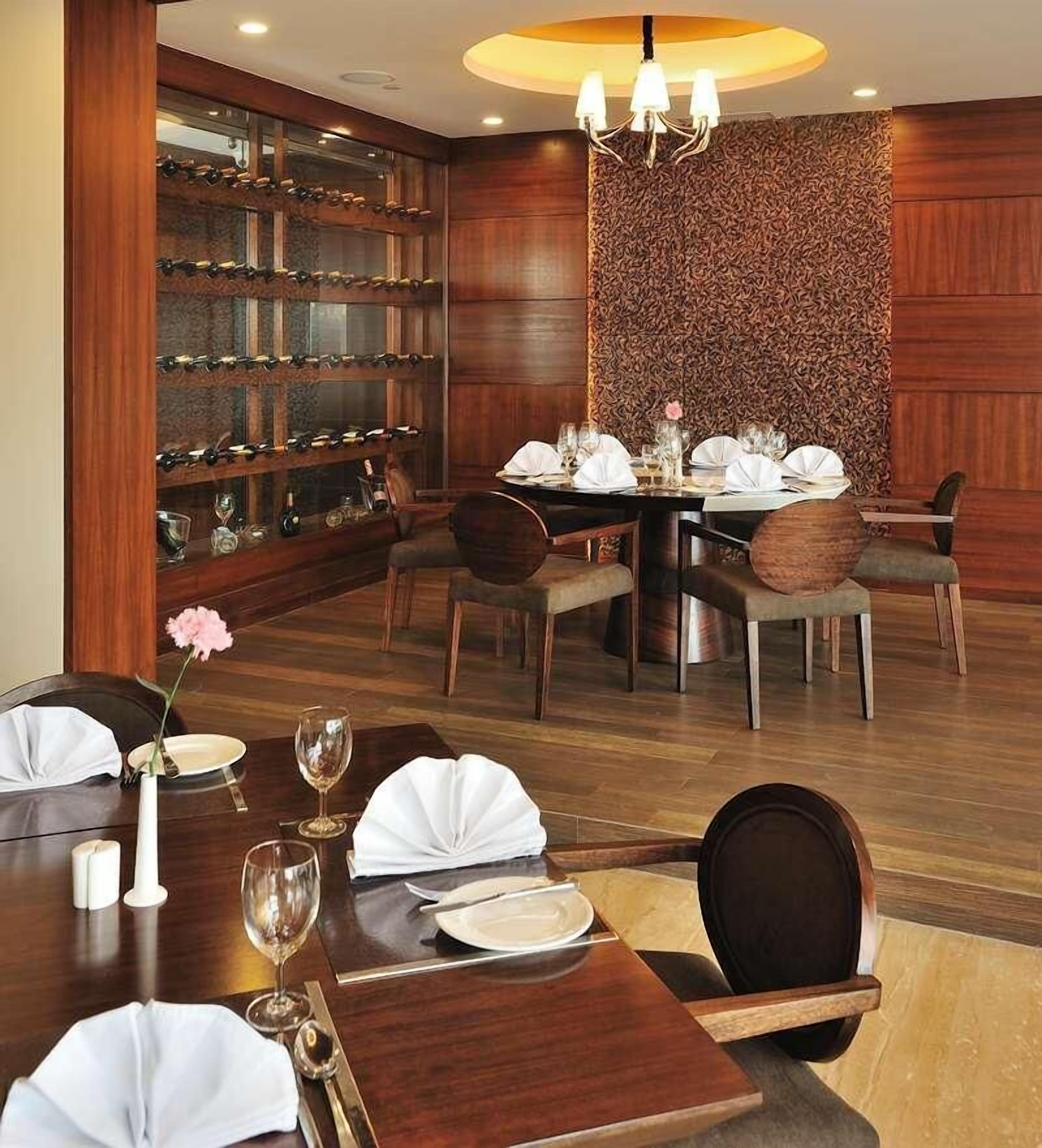 A dining area with a round table set for four, surrounded by wooden chairs. A wine rack with bottles is visible in the background.