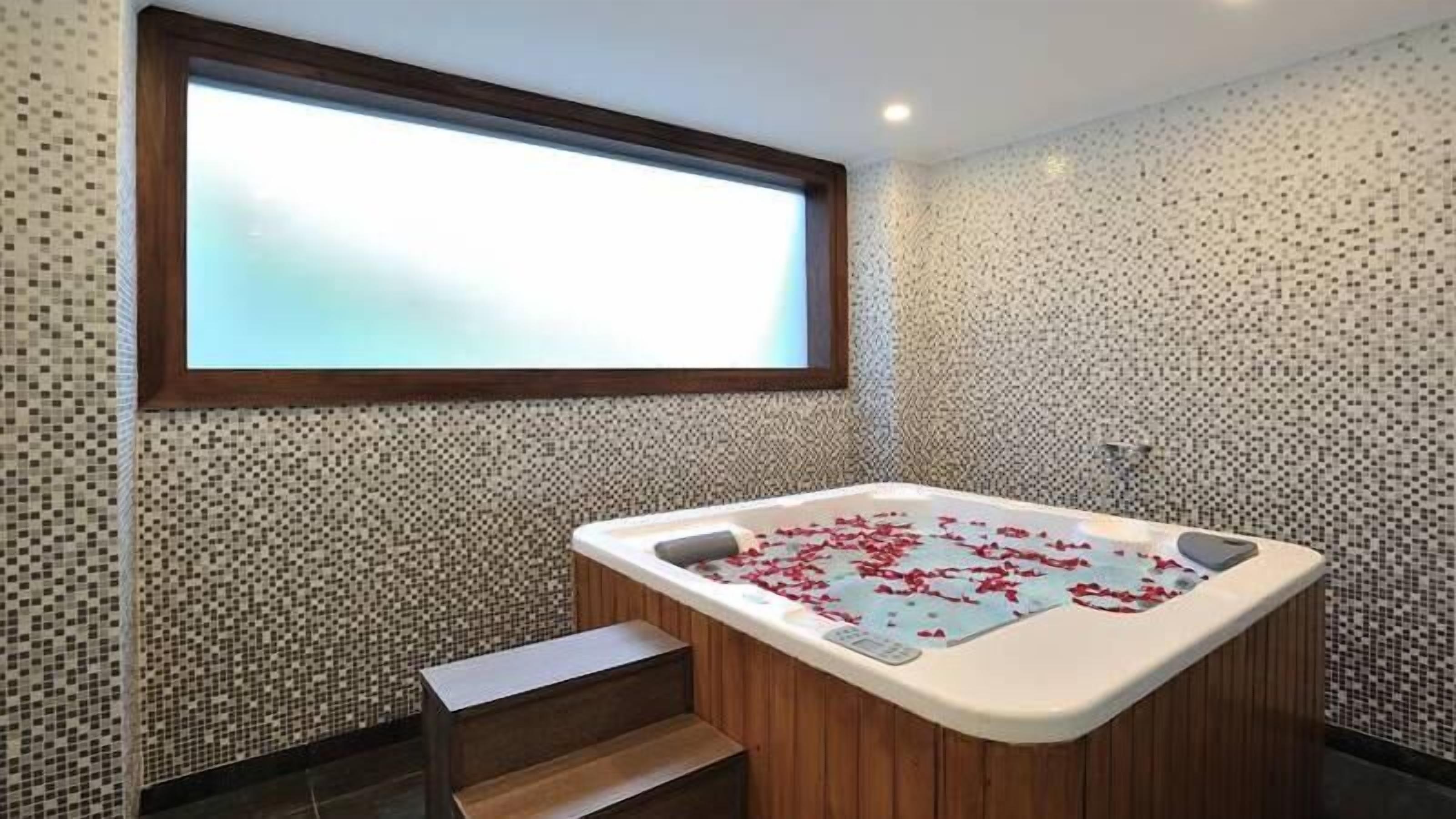 Ein modernes Badezimmer mit einer freistehenden Badewanne, einer kleinen Holzbank und einem großen Fenster über der Wanne.