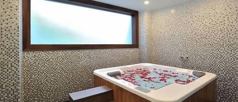 Ein modernes Badezimmer mit einer freistehenden Badewanne, einer kleinen Holzbank und einem großen Fenster über der Wanne.