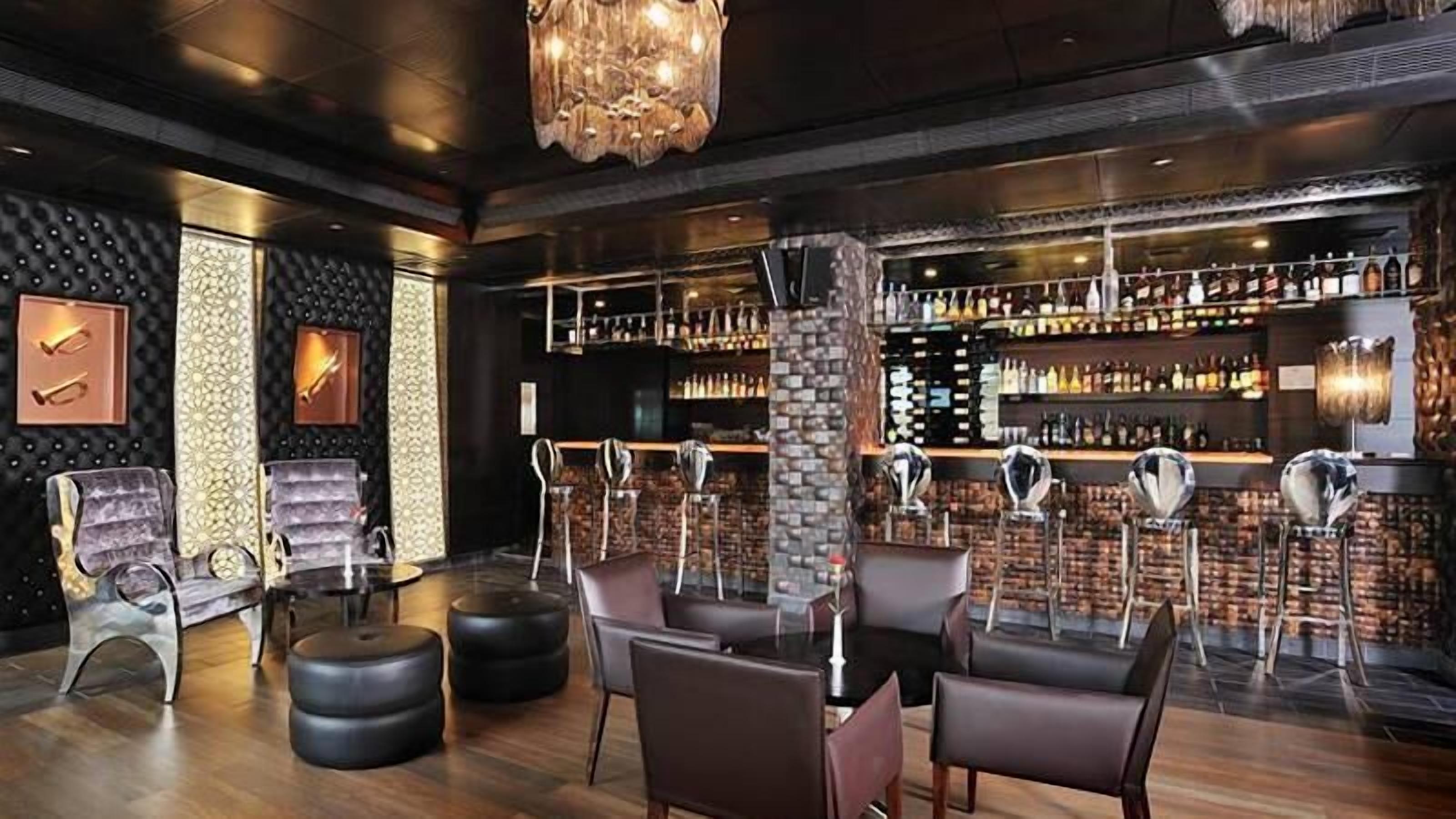 A bar area with leather chairs, a stone pillar, and a variety of bottles on shelves.
