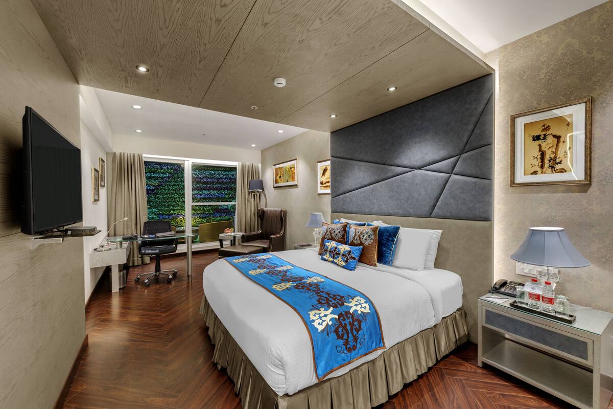 Habitación de hotel moderna con una cama grande, un escritorio, un televisor y vistas a zonas verdes por la ventana.