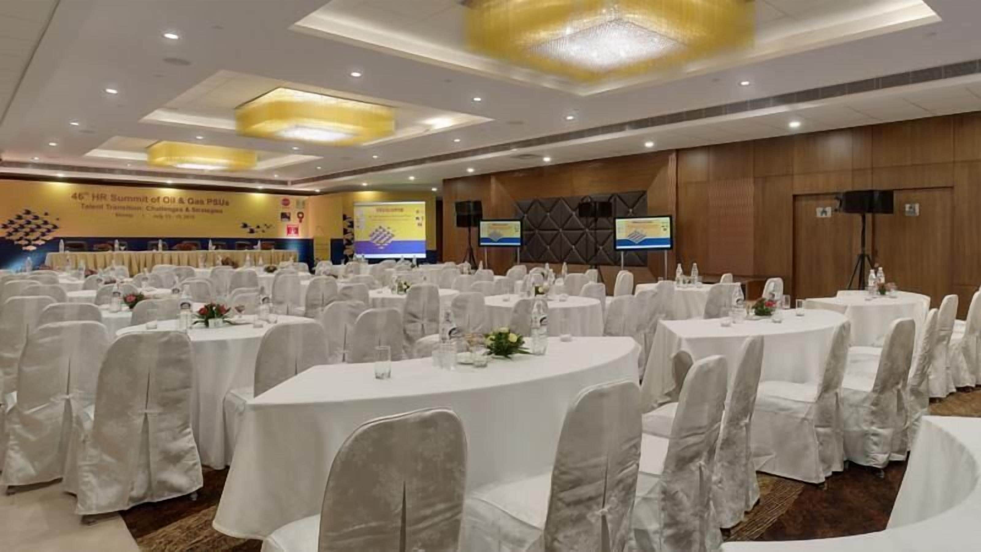 Ein Konferenzraum mit runden Tischen und weißen Stühlen, ausgestattet mit Wasserflaschen und floralen Tischdekorationen.