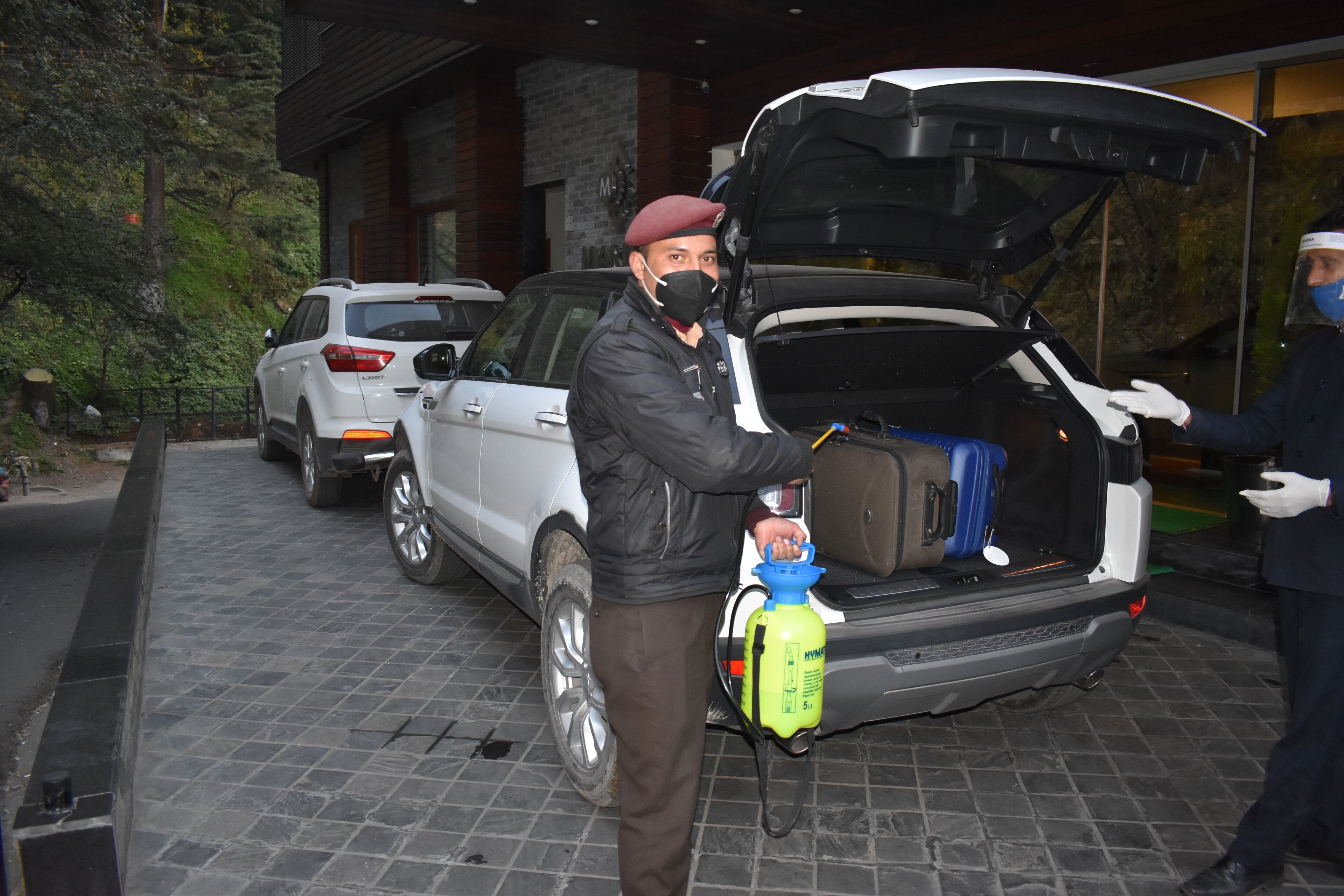Un vehículo con el maletero abierto, se observa equipaje en su interior, y una persona manipulando una botella de limpiador.