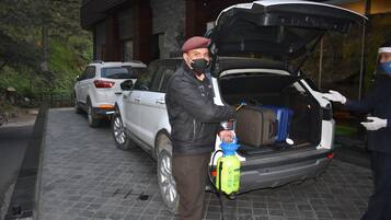 Un vehículo con el maletero abierto, se observa equipaje en su interior, y una persona manipulando una botella de limpiador.