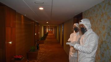 A hotel corridor with wooden paneling, potted plants, and a patterned carpet.