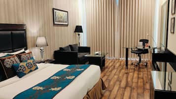 A hotel room with a large bed, a desk, a chair, a lamp, and a TV.