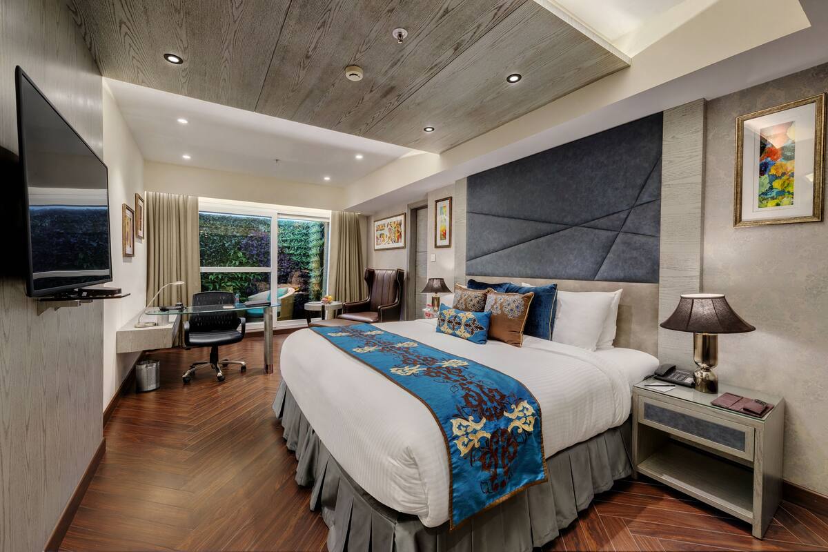 Una habitación de hotel moderna con una cama grande, un escritorio, un televisor y vistas a zonas verdes.
