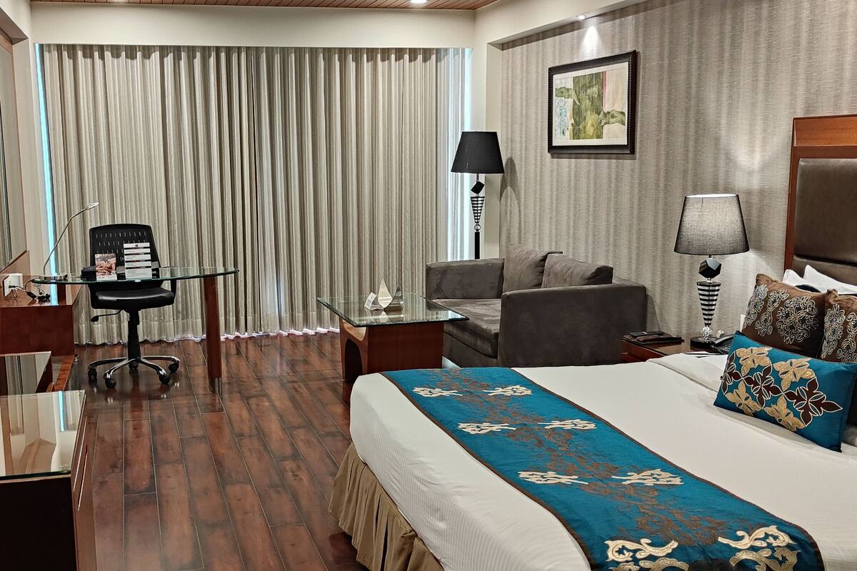 Una habitación de hotel con cama, escritorio y silla, televisión y ventana con cortinas.