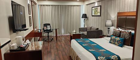 A hotel room with a bed, a desk with a chair, a TV, and a window with curtains.