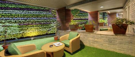 A modern indoor garden with a brick wall, green artificial grass, and wicker furniture.