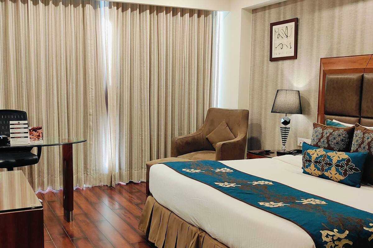 Una habitación de hotel con una cama, un escritorio con computadora, una silla, una lámpara y un televisor.
