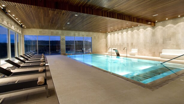 Une piscine intérieure avec des parois en verre transparent, un plafond en bois et une vue sur les montagnes environnantes.