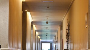Un long couloir étroit, doté d’un tapis sombre, de portes en bois et d’une table sur laquelle se trouve un vase, le tout situé sur le côté droit.