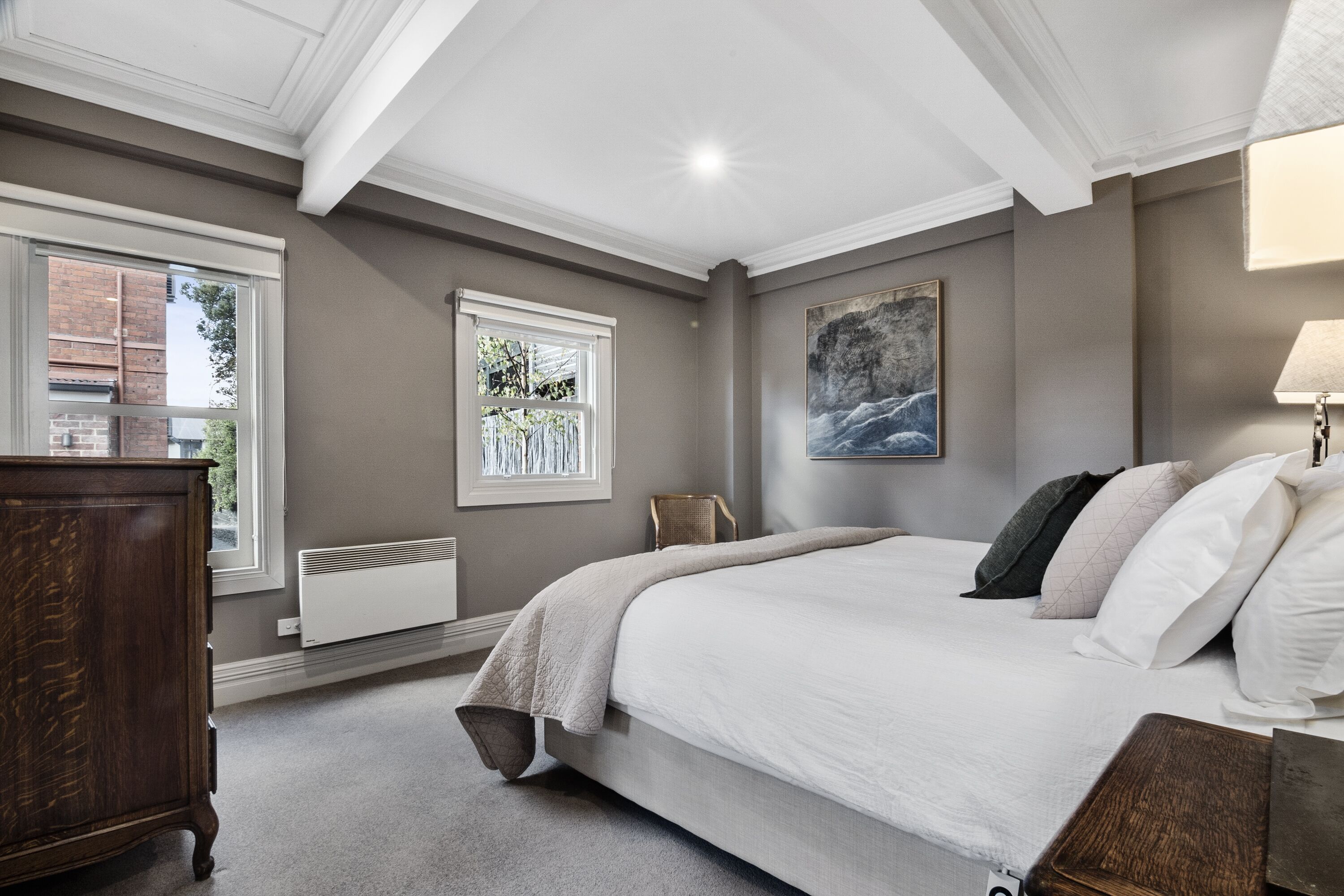A bedroom with a large bed, a dresser, a radiator, and a window with a view of trees.