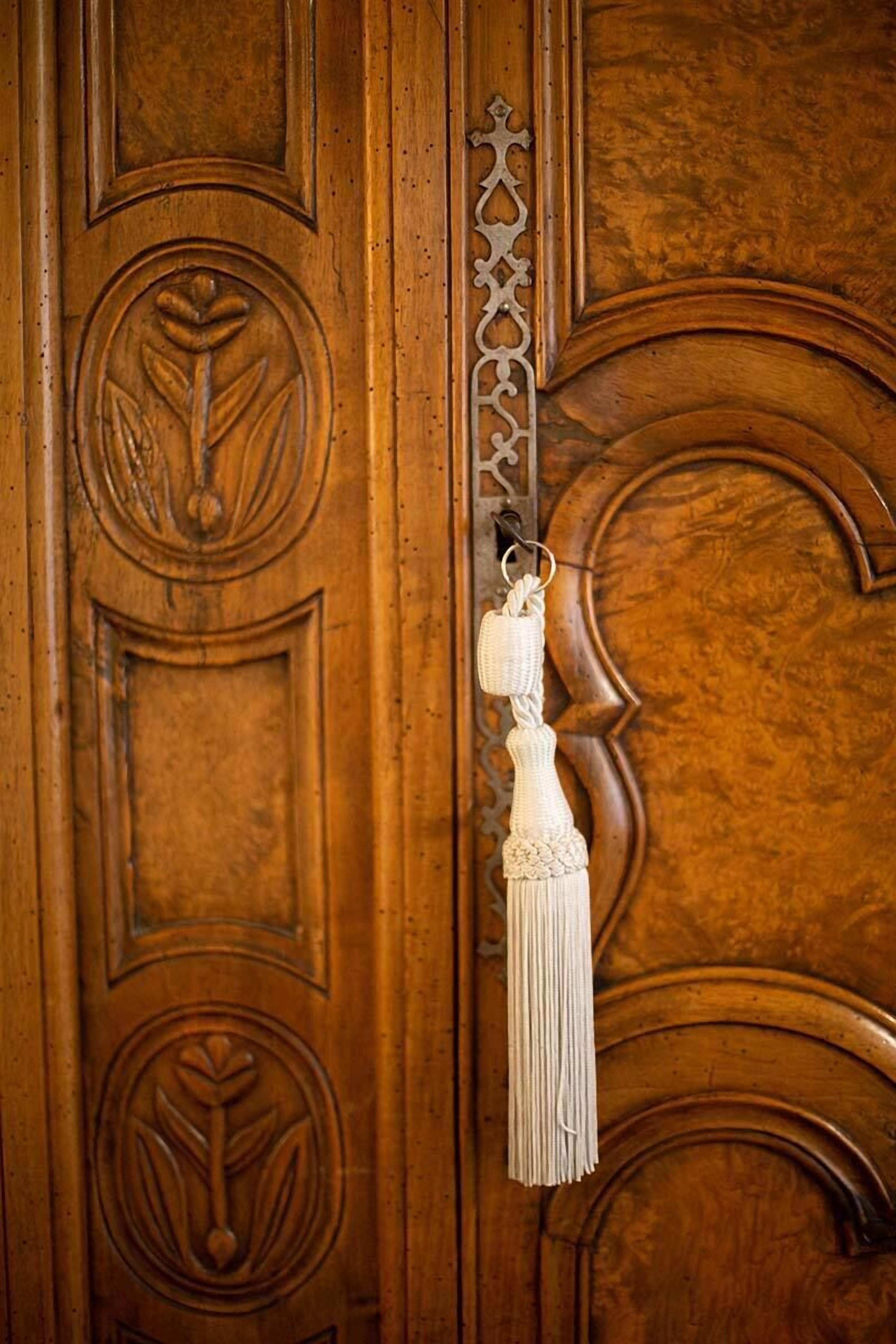 A wooden door with intricate carvings and a white tassel hanging from a keyhole.