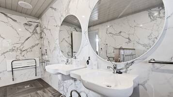 A modern bathroom with marble walls, two sinks, a shower, and a wooden floor.