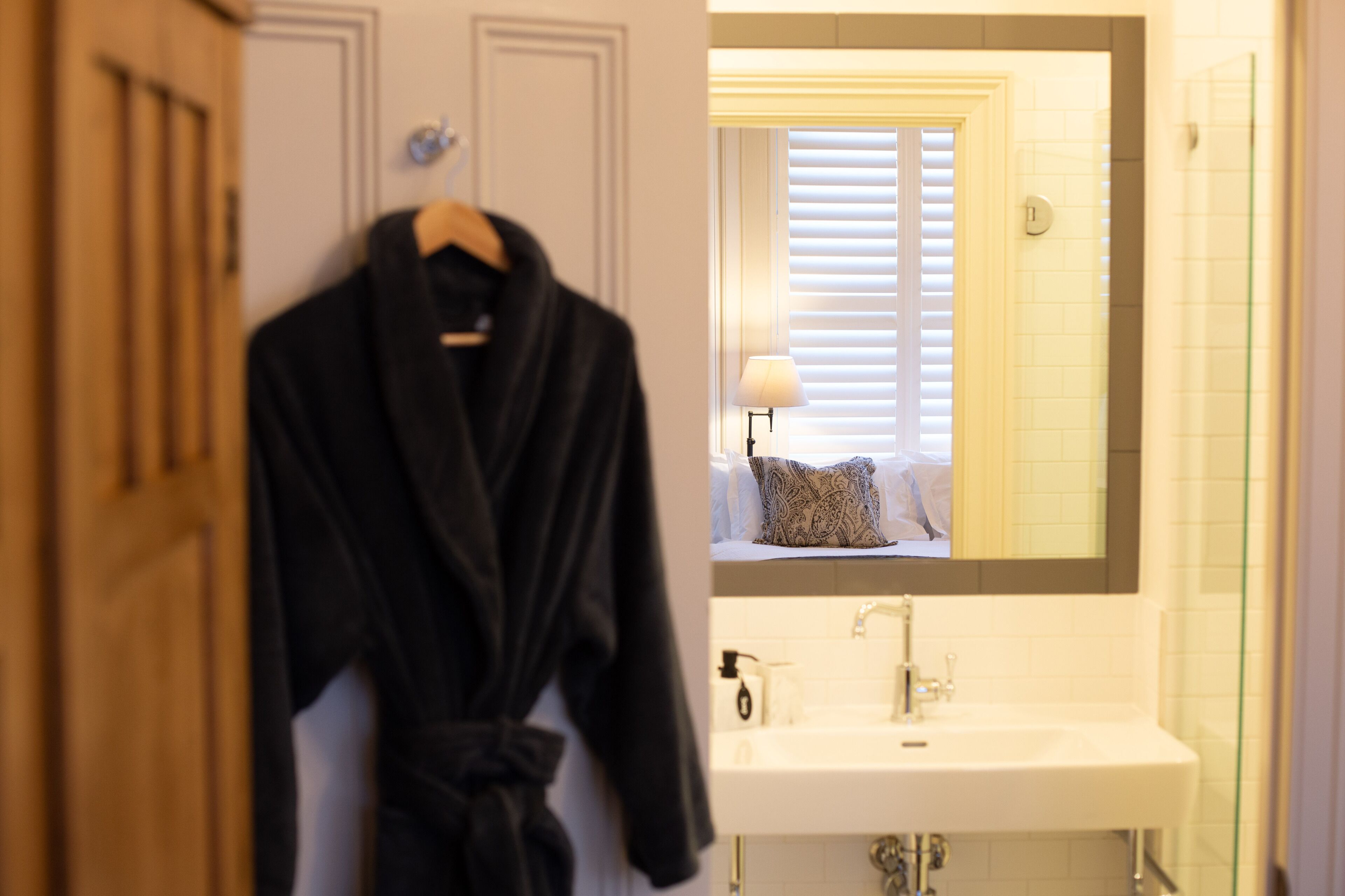 A bathroom with a white sink, a mirror, and a robe hanging on a door.