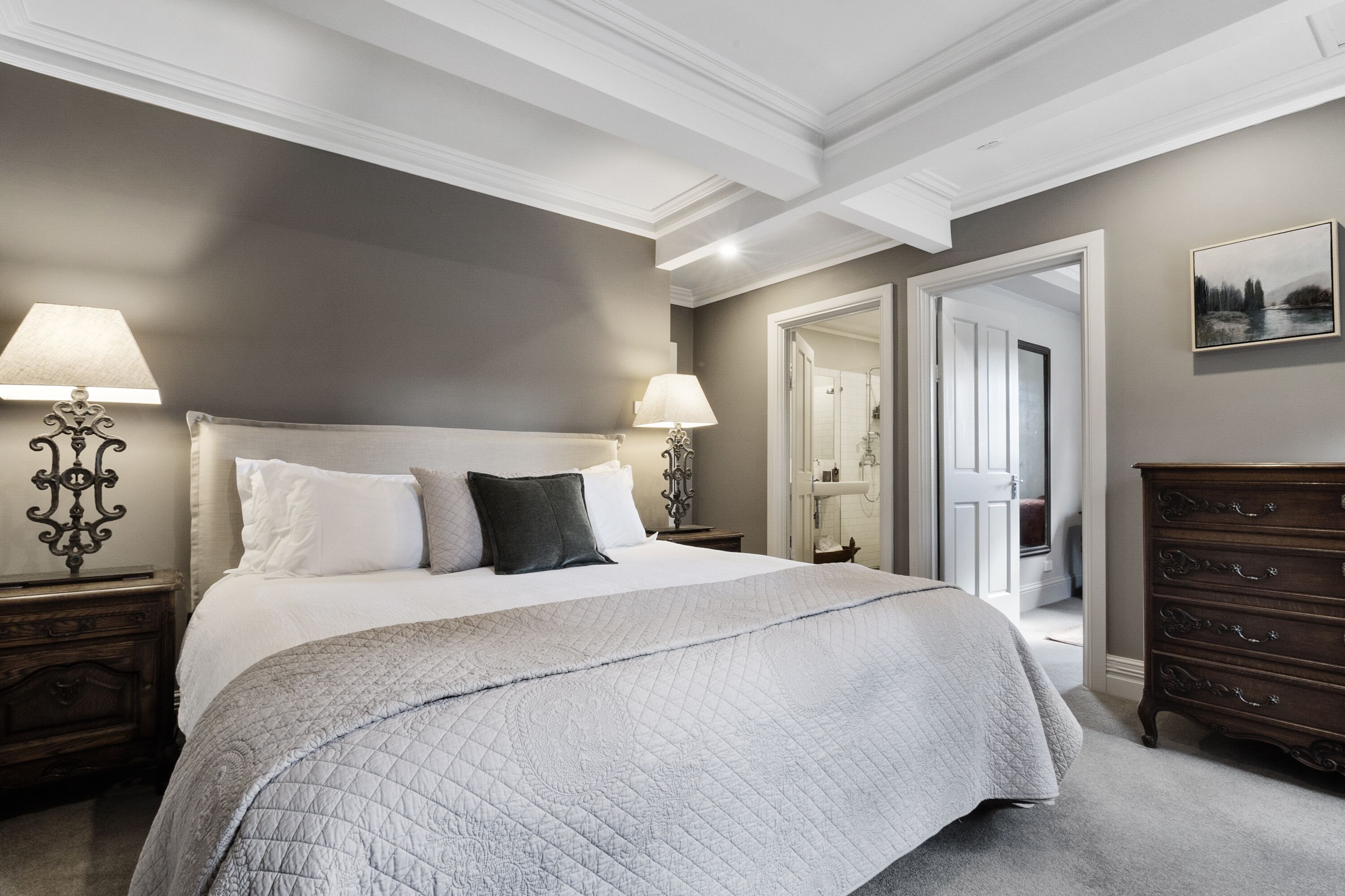 Een slaapkamer met een groot bed, twee nachtkastjes met lampen, een dressoir en een deur naar een andere kamer.