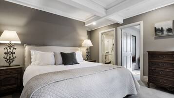 Een slaapkamer met een groot bed, twee nachtkastjes met lampen, een dressoir en een deur naar een andere kamer.