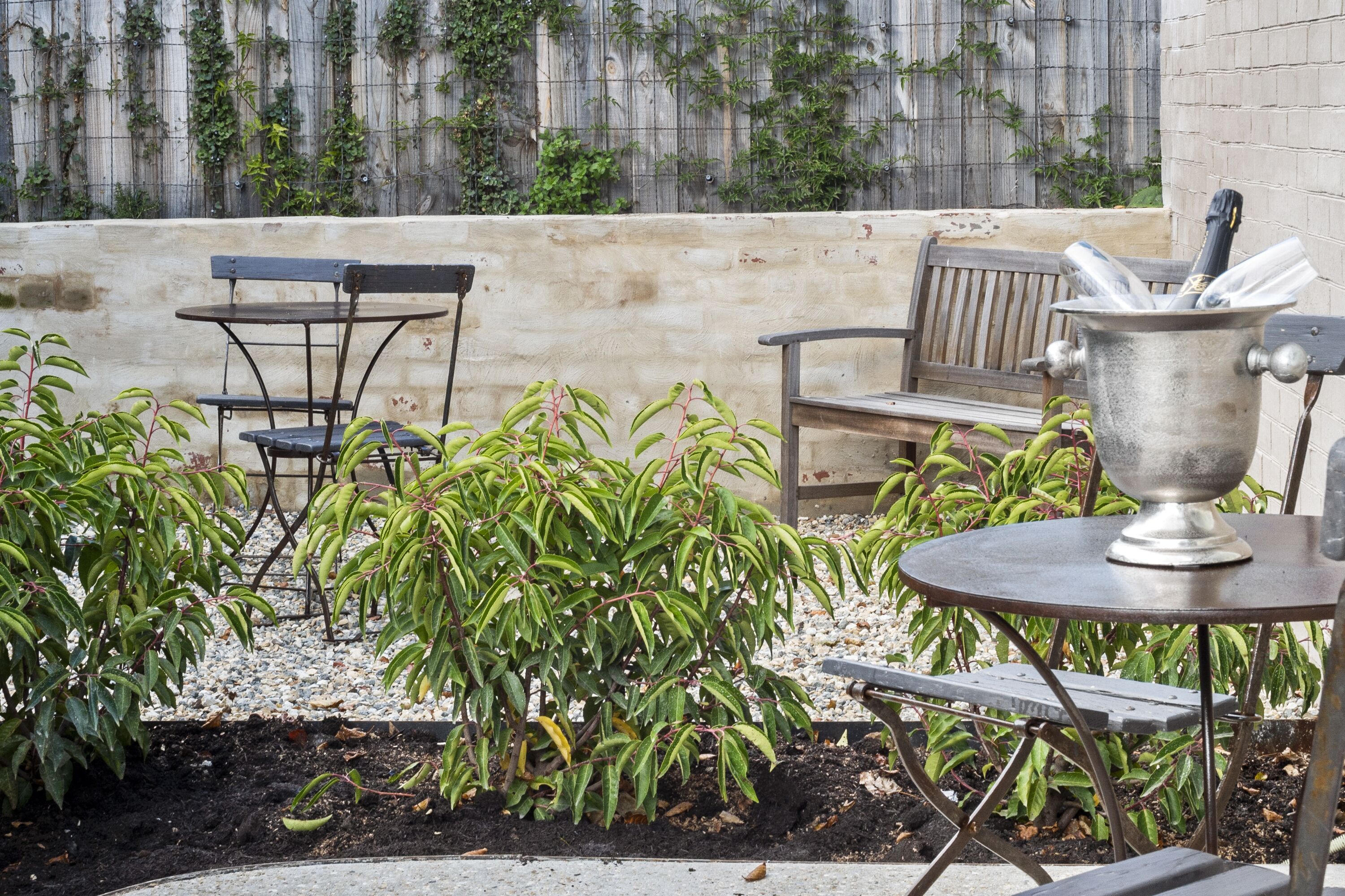 A patio area with a metal table, a bench, and a planter with green plants.
