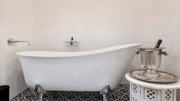 A clawfoot bathtub in a bathroom with white tiled walls and a patterned floor.