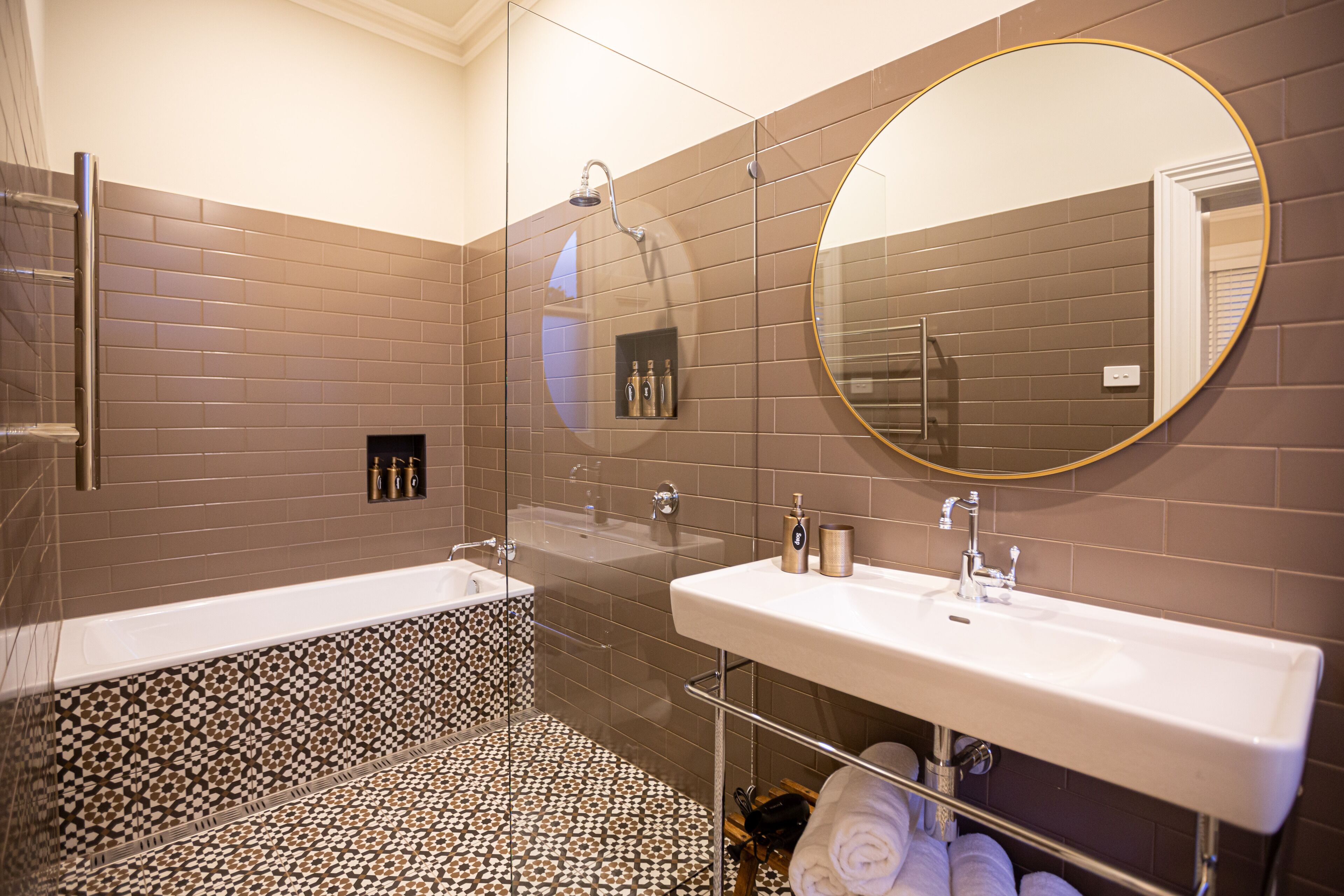 Un baño moderno con ducha envuelta en vidrio, tocador doble y baldosas de suelo con diseño.