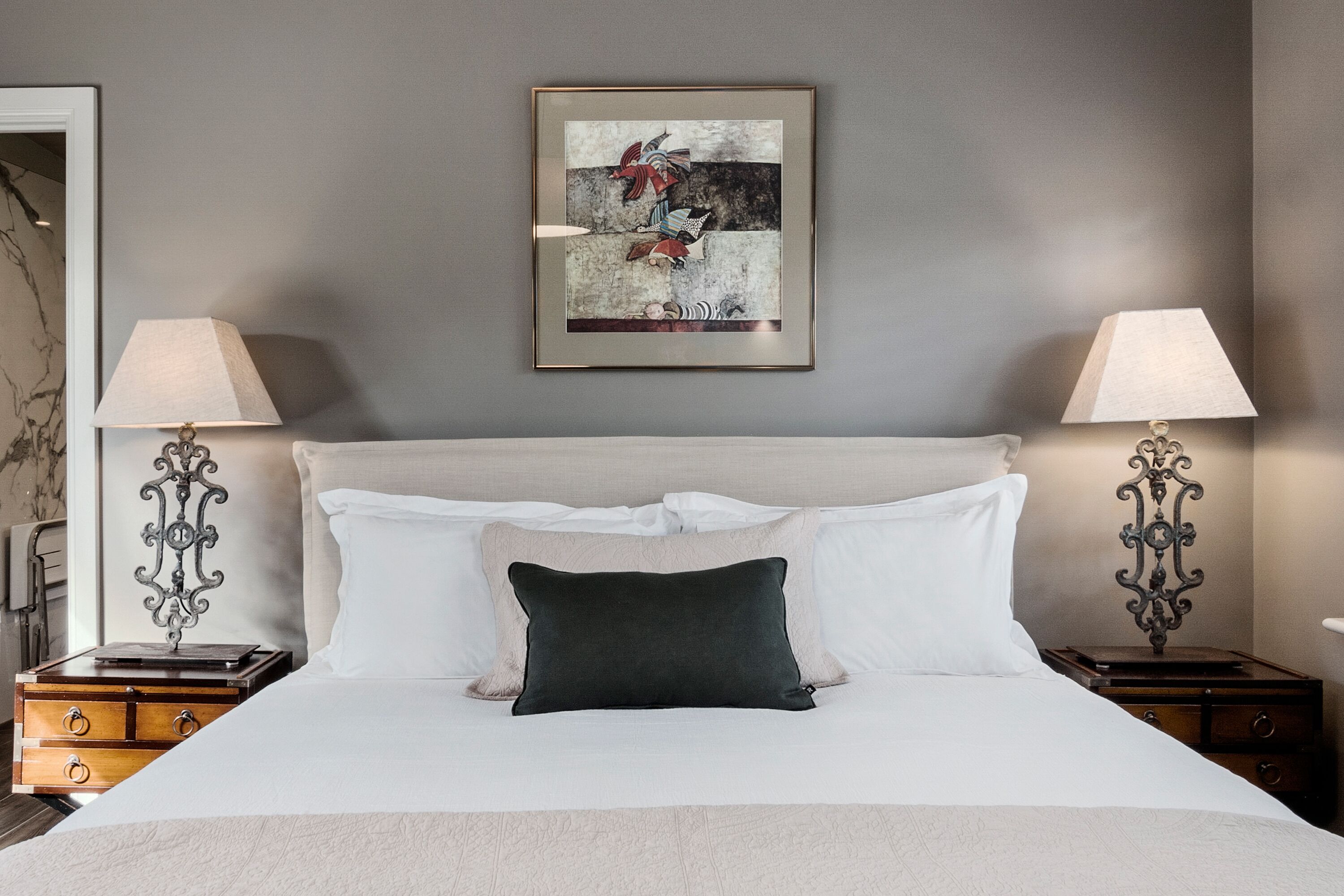 A neatly made bed with a dark pillow, two bedside tables with lamps, and a framed picture on the wall.