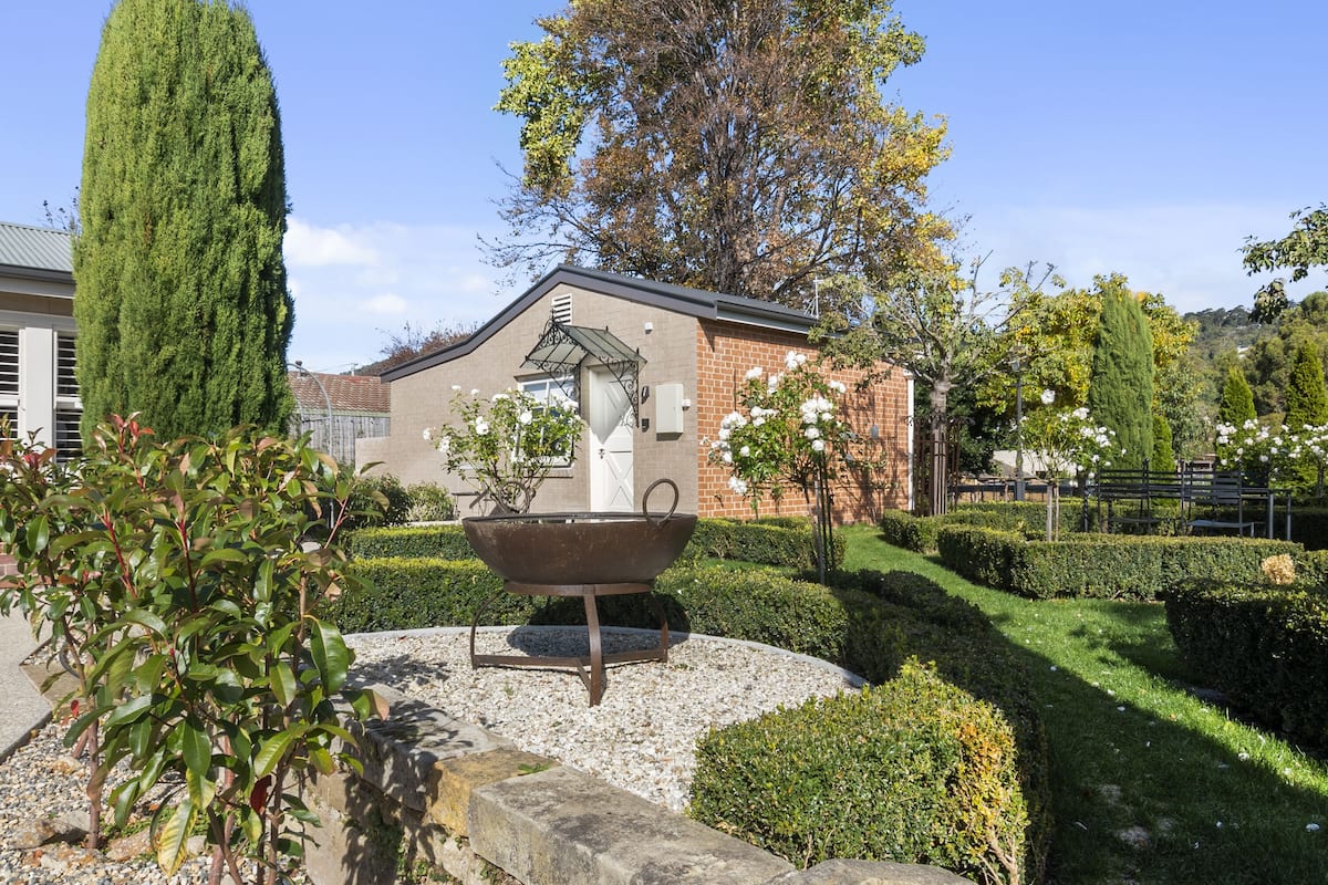 Un jardín con una gran cuenca metálica, setos podados y un árbol alto.