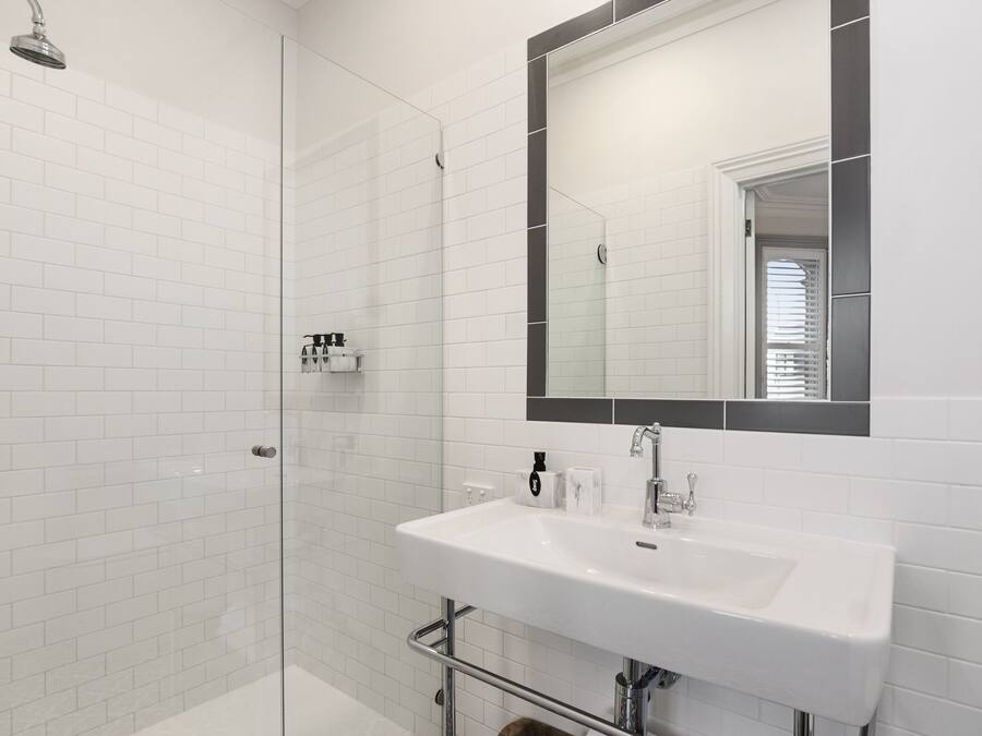 Une salle de bain moderne avec une douche à l’italienne en verre, un lavabo blanc avec un grand miroir et des carreaux de métro blancs sur les murs.