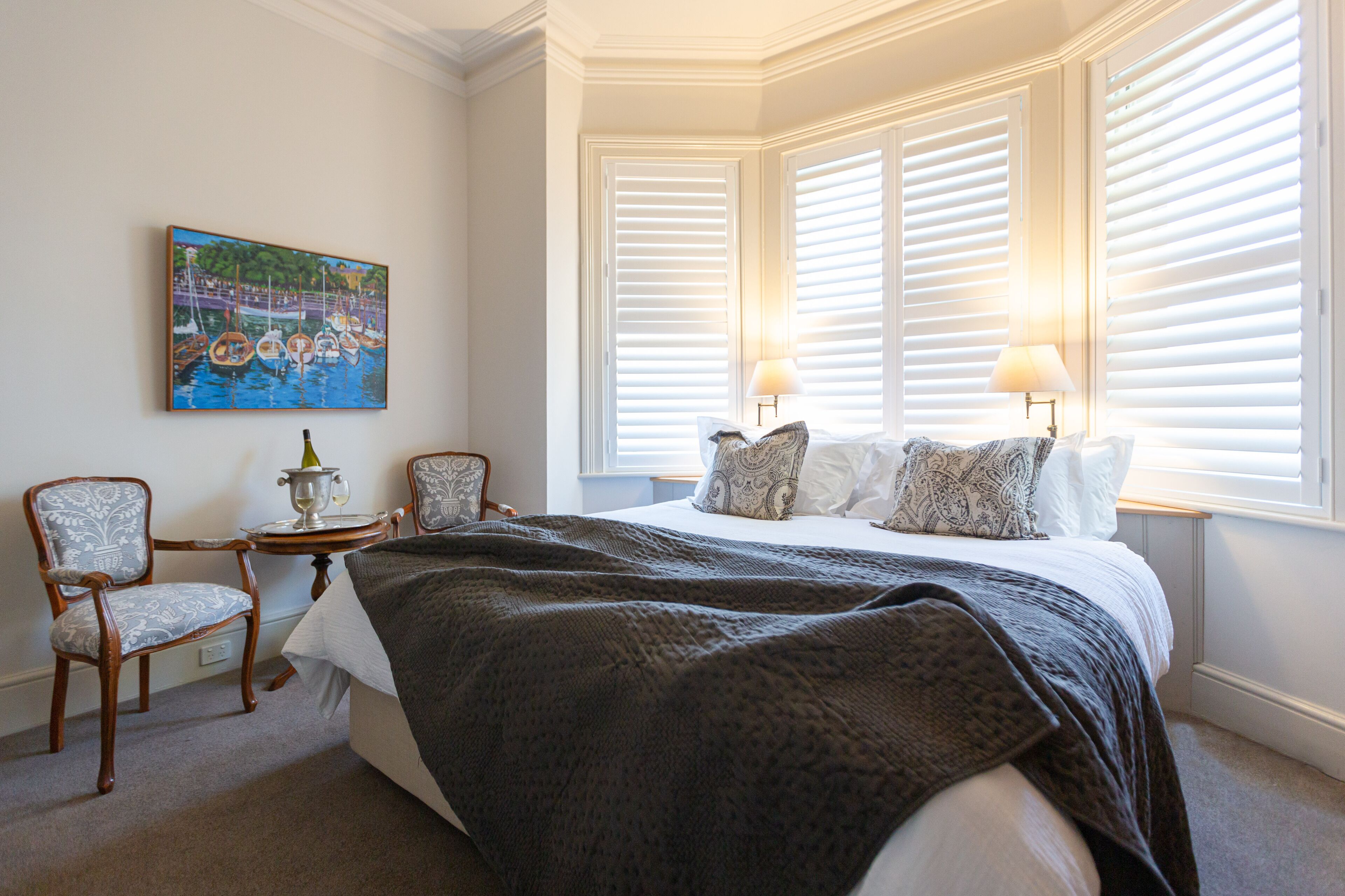 Une chambre à coucher avec un grand lit, deux chaises, une petite table avec une lampe et un tableau au mur.