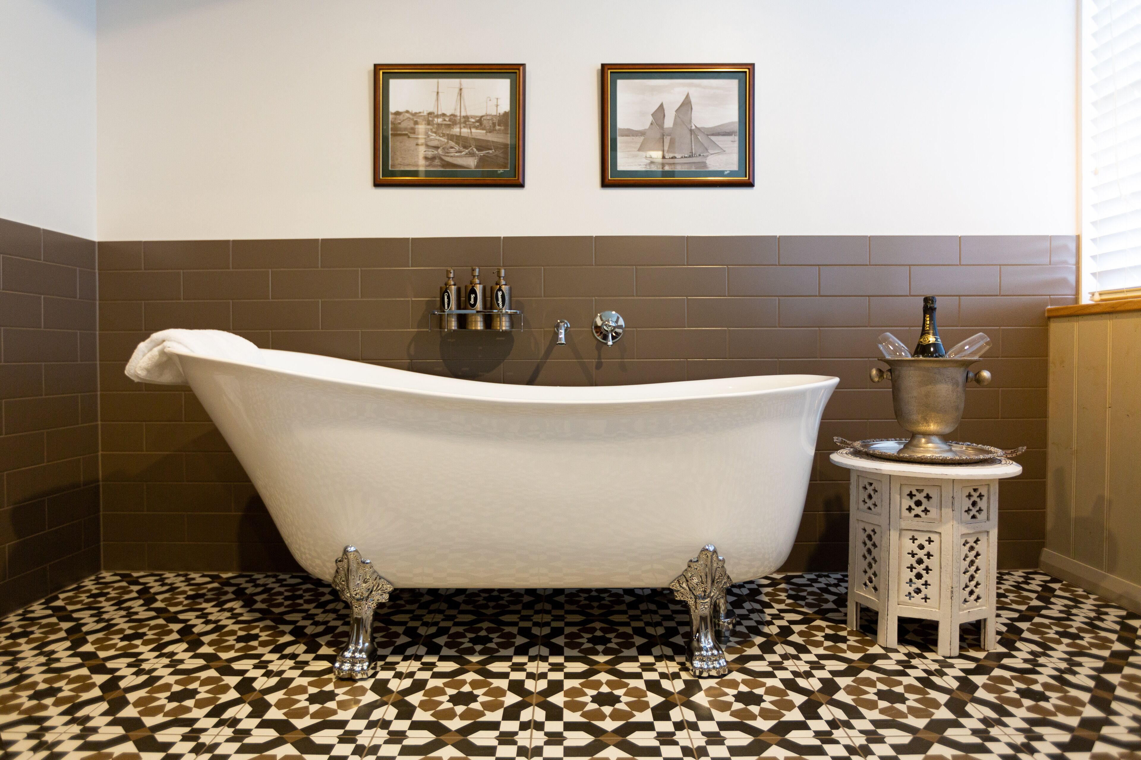 A bathroom with a freestanding bathtub, two framed pictures on the wall, and a tiled floor.
