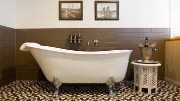 A bathroom with a freestanding bathtub, two framed pictures on the wall, and a tiled floor.