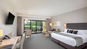 A hotel room with a large bed, a desk, a chair, a TV mounted on the wall, and a view of the outdoors through a sliding glass door.