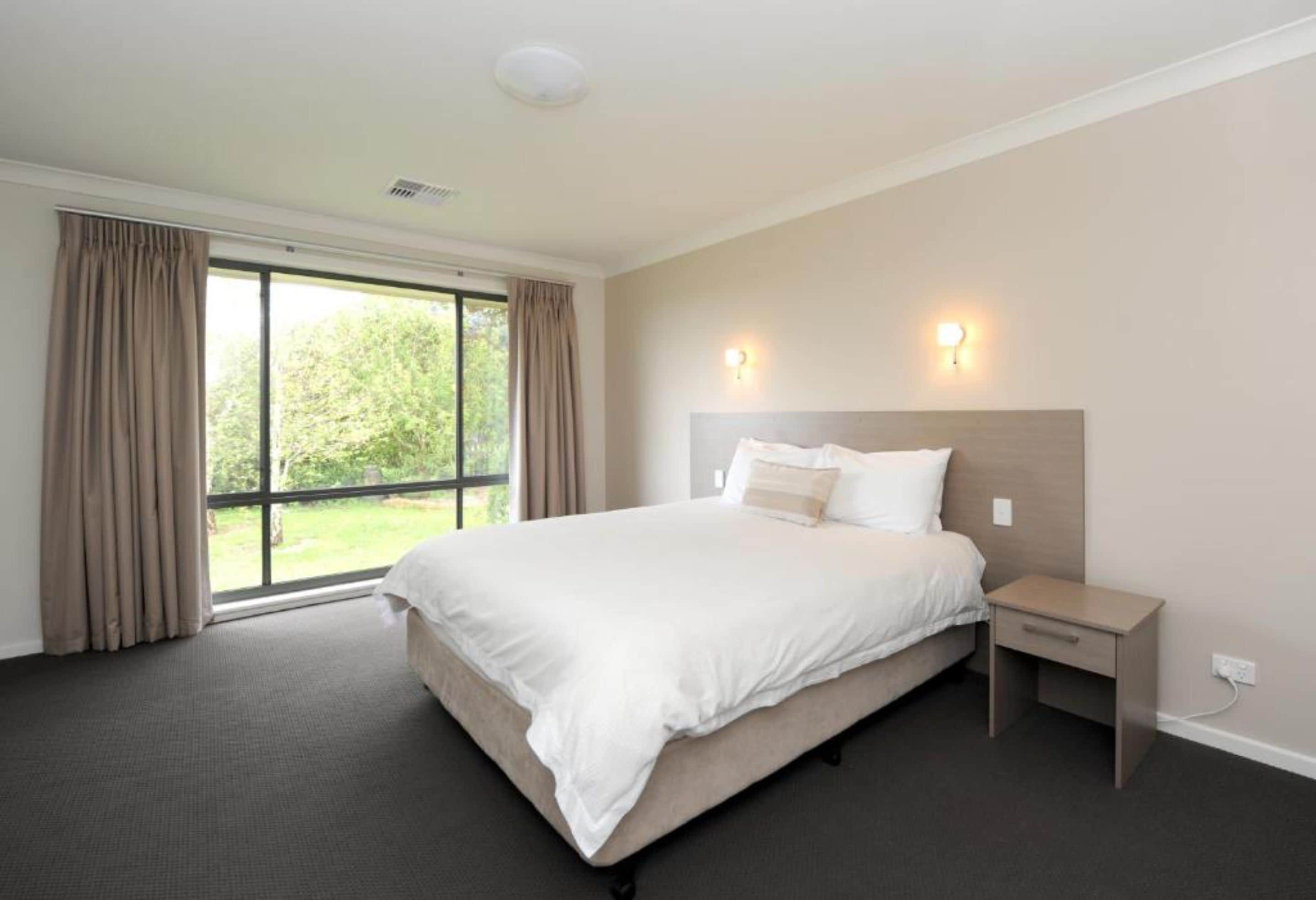 A hotel room with a large bed, a bedside table, and a window with curtains.
