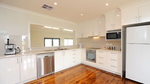 A modern kitchen with white cabinets, stainless steel appliances, and a wooden floor. - The Barn Accommodation (Ob Flat)