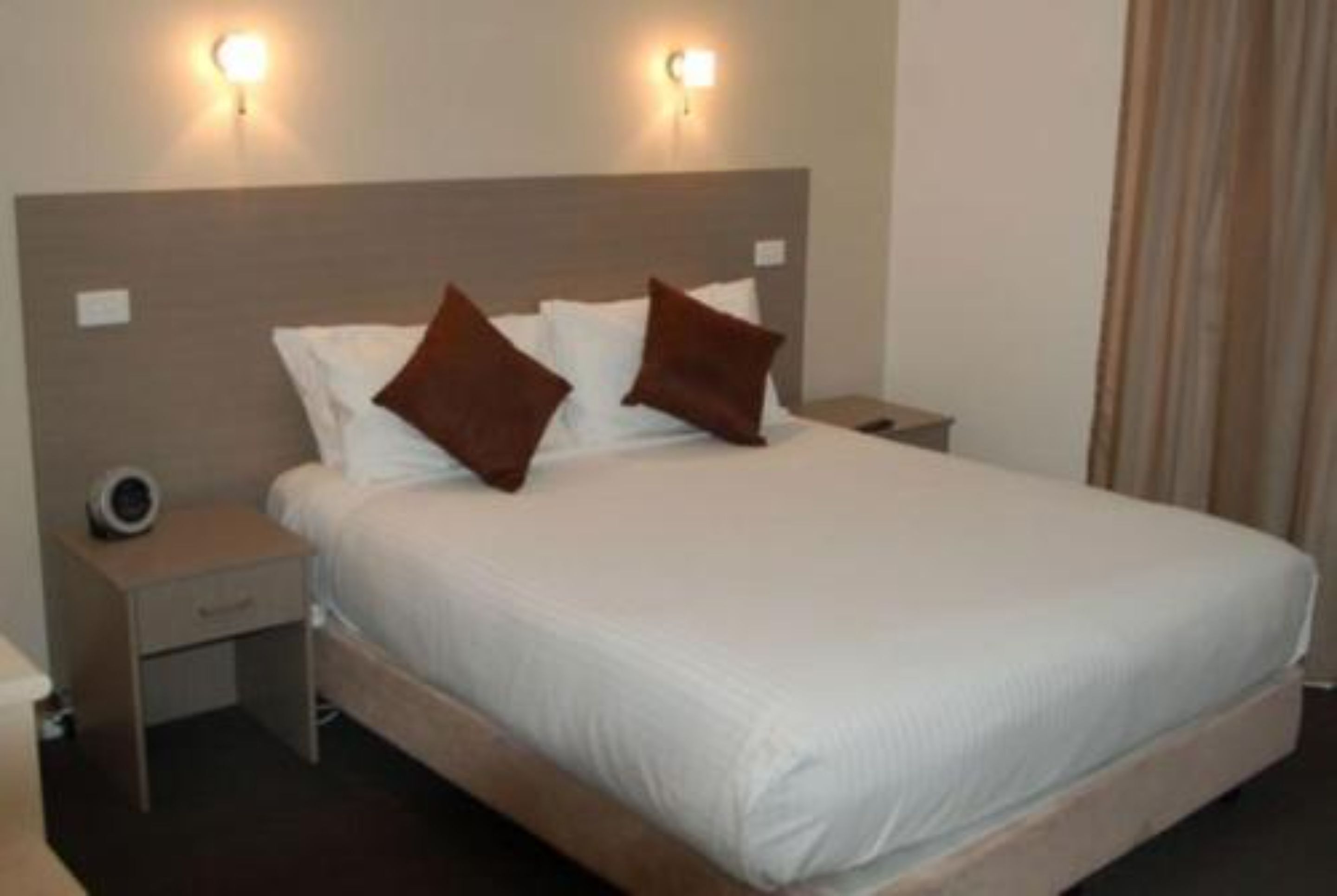 A hotel room with a large bed, two bedside tables, and wall-mounted lights.