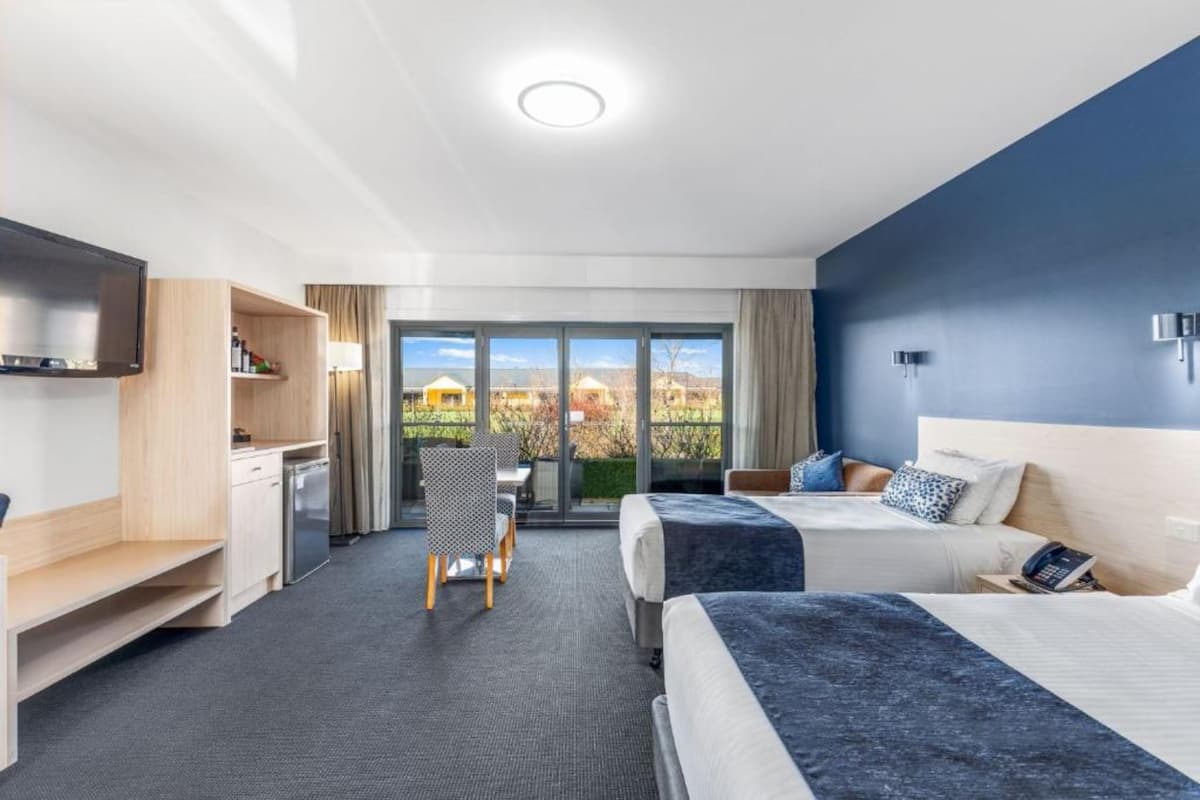 Hotellihuone, jossa on kaksi sänkyä, työpöytä, tuoli, televisio ja parveke, jolta on näkymä.