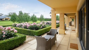 A covered outdoor area with a patio, two wicker chairs, and a garden with pink flowers. - The Barn Accommodation (Ob Flat)