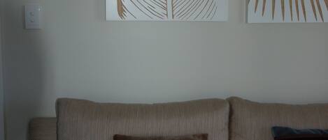 A beige sofa with three cushions in shades of brown and green, and two leaf-patterned artworks on the wall.
