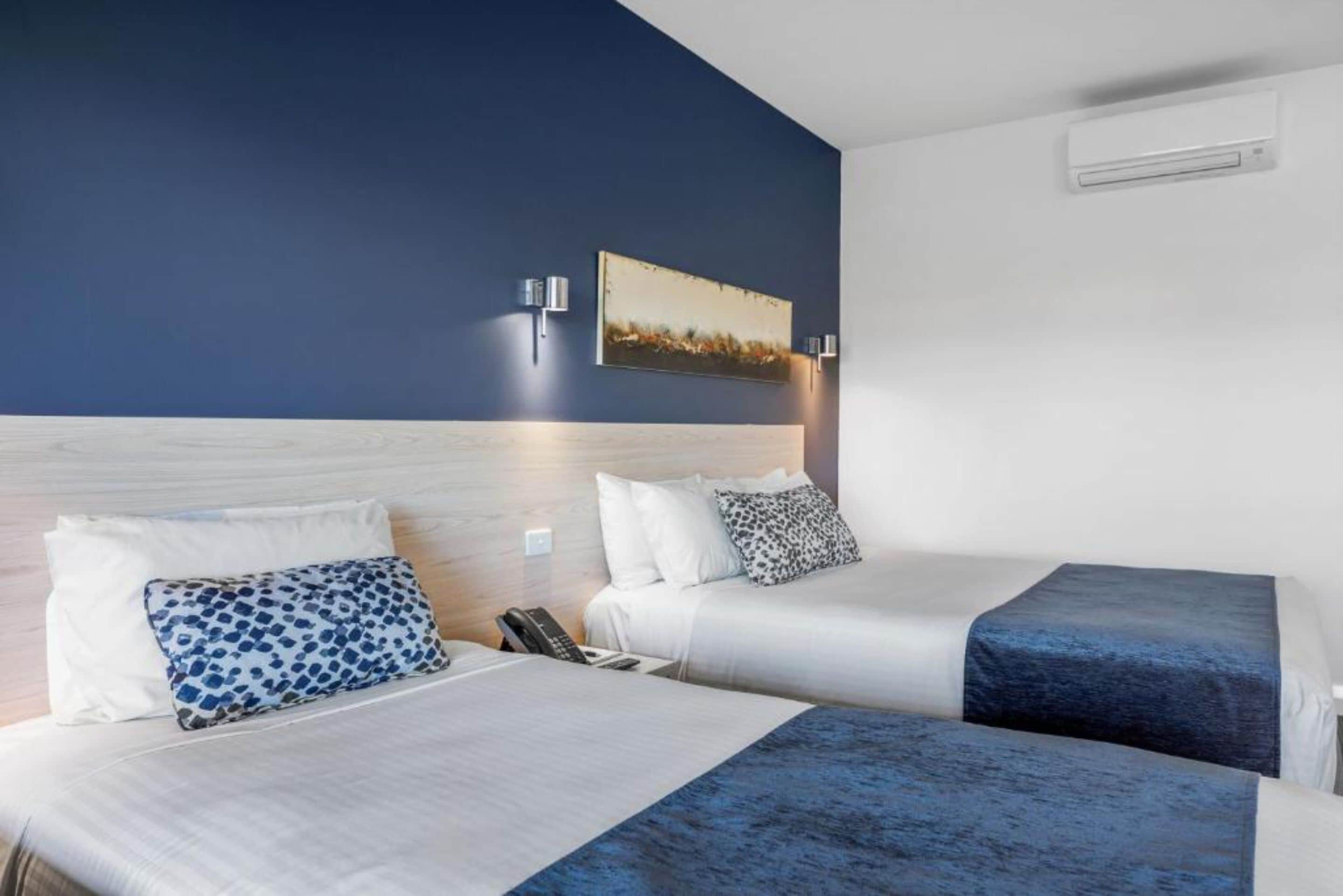 A hotel room with two beds, a wooden headboard, a painting on the wall, and an air conditioning unit.
