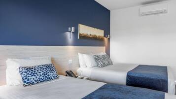 A hotel room with two beds, a wooden headboard, a painting on the wall, and an air conditioning unit.
