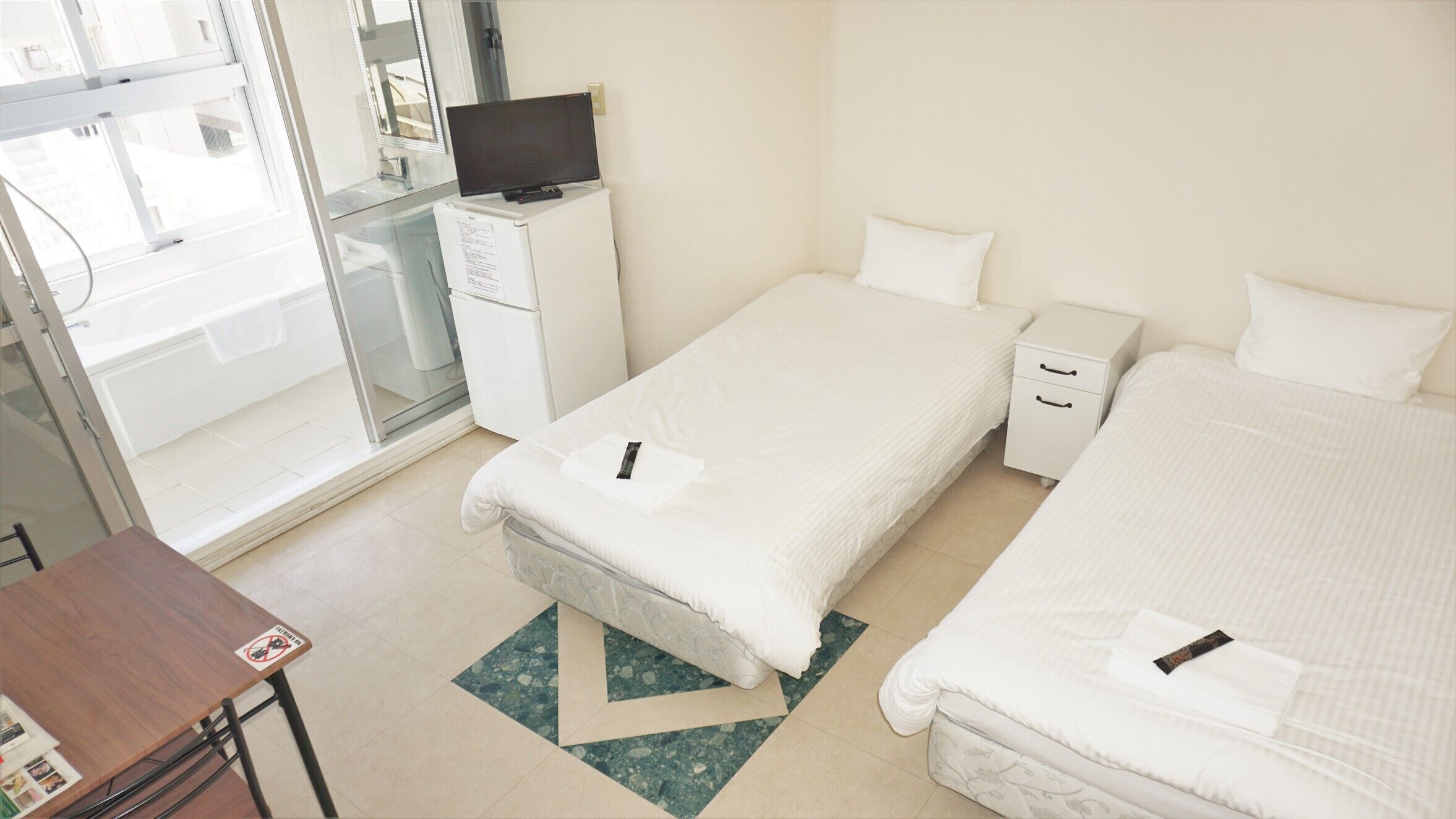 A hotel room with two beds, a desk, a television, and a bathroom with a glass door.