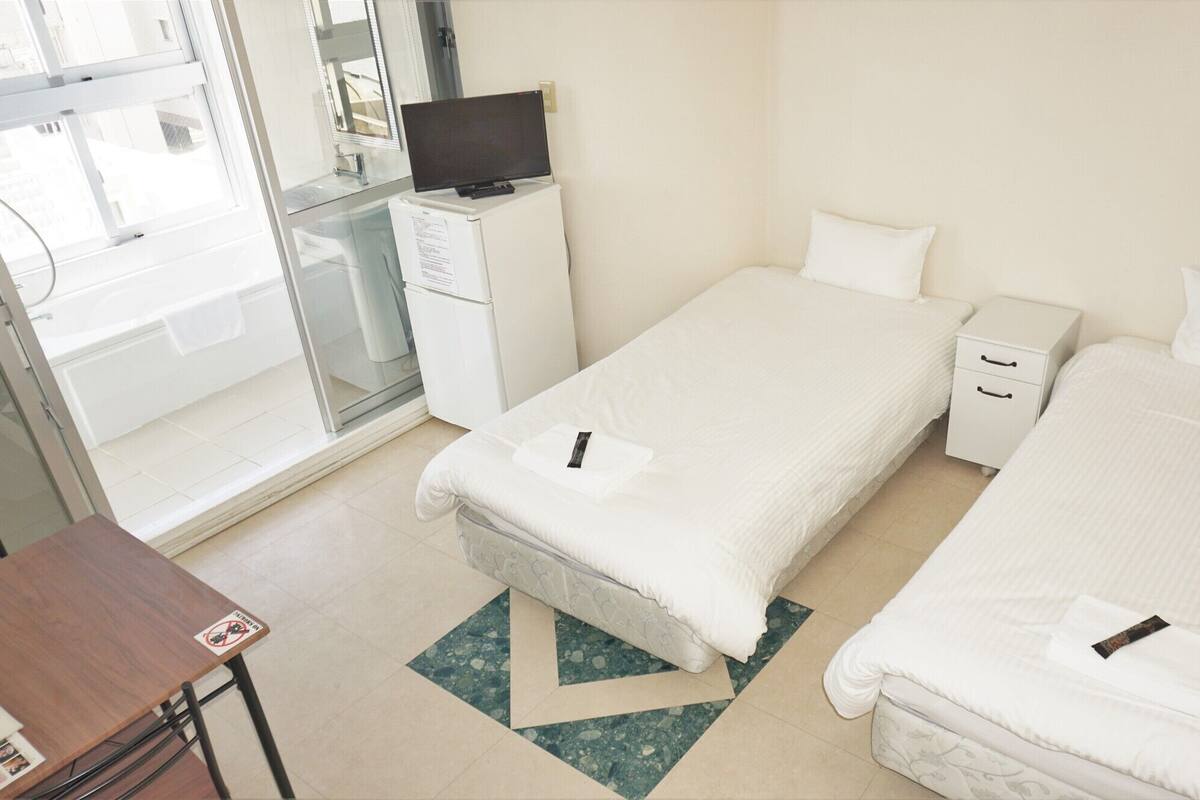 A hotel room with two beds, a desk, a television, and a bathroom with a glass door.