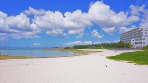 A beach with a white sandy shore, a clear blue sky, and a large building in the background. - Okinawa Ocean Front Hotel  (Chatan)