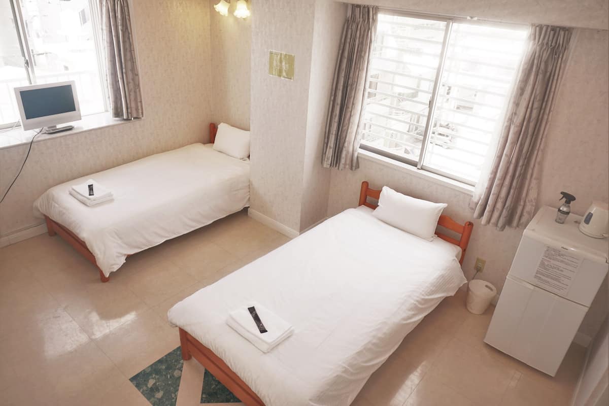 A hotel room with two single beds, a small desk with a computer, a washing machine, and a window with curtains.