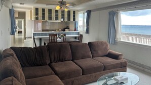 A living room with a brown sofa, a glass coffee table, and a view of the sea through large windows. - Okinawa Ocean Front Hotel  (Chatan)