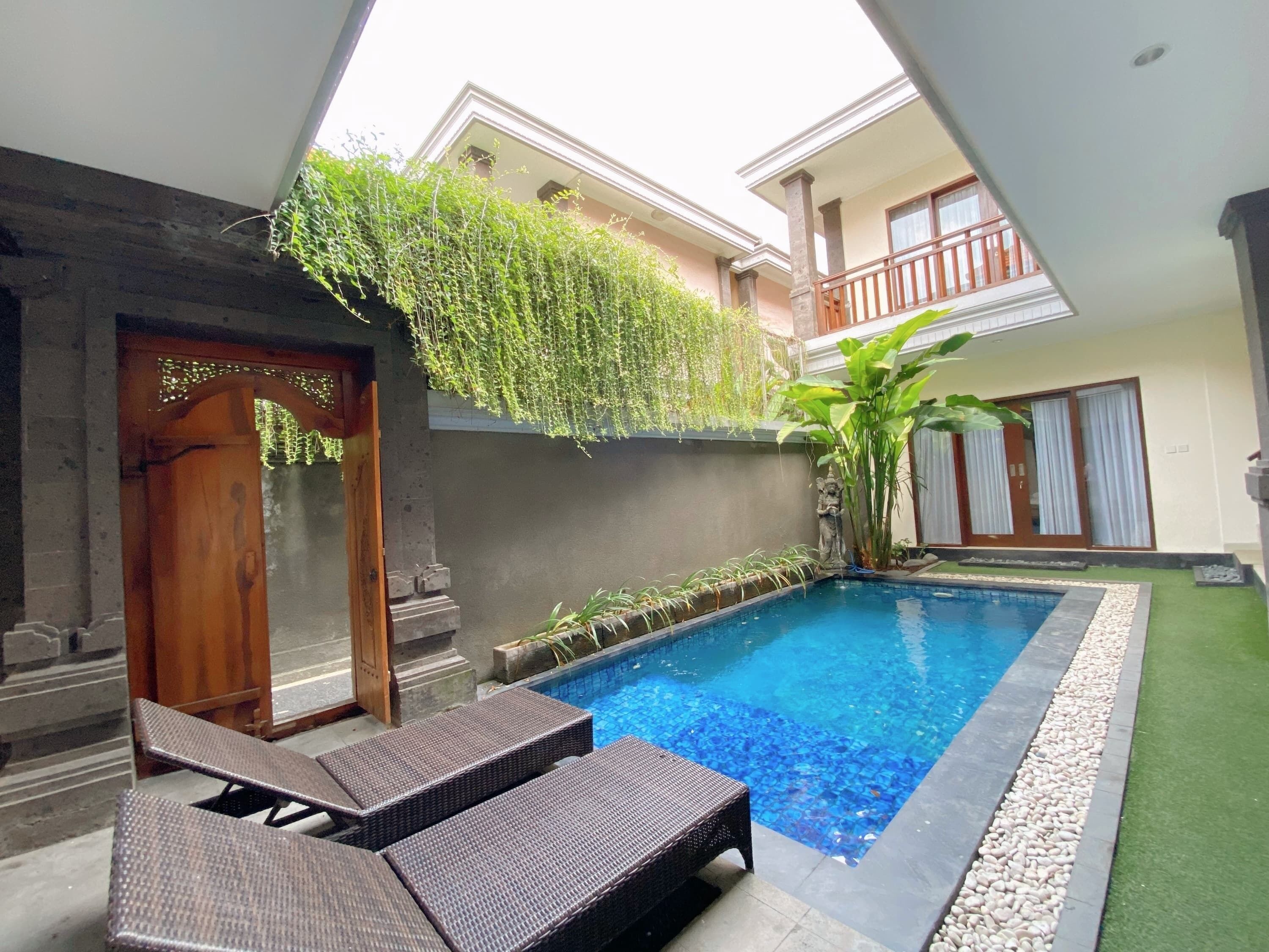 A swimming pool with lounge chairs, a stone wall, and a balcony with plants.