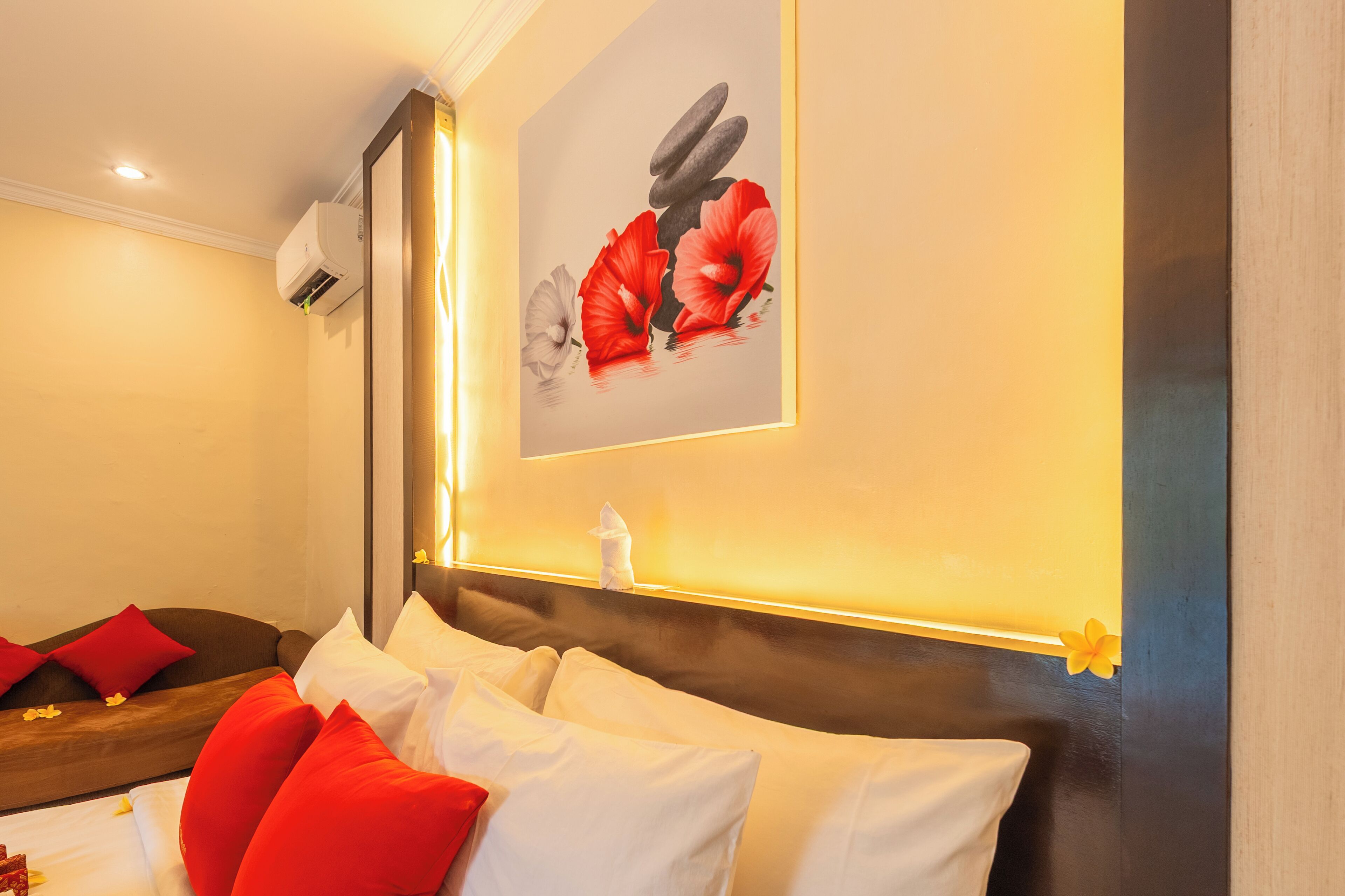 Una camera d'hotel con un letto, cuscini, un condizionatore d'aria a parete e un quadro incorniciato.