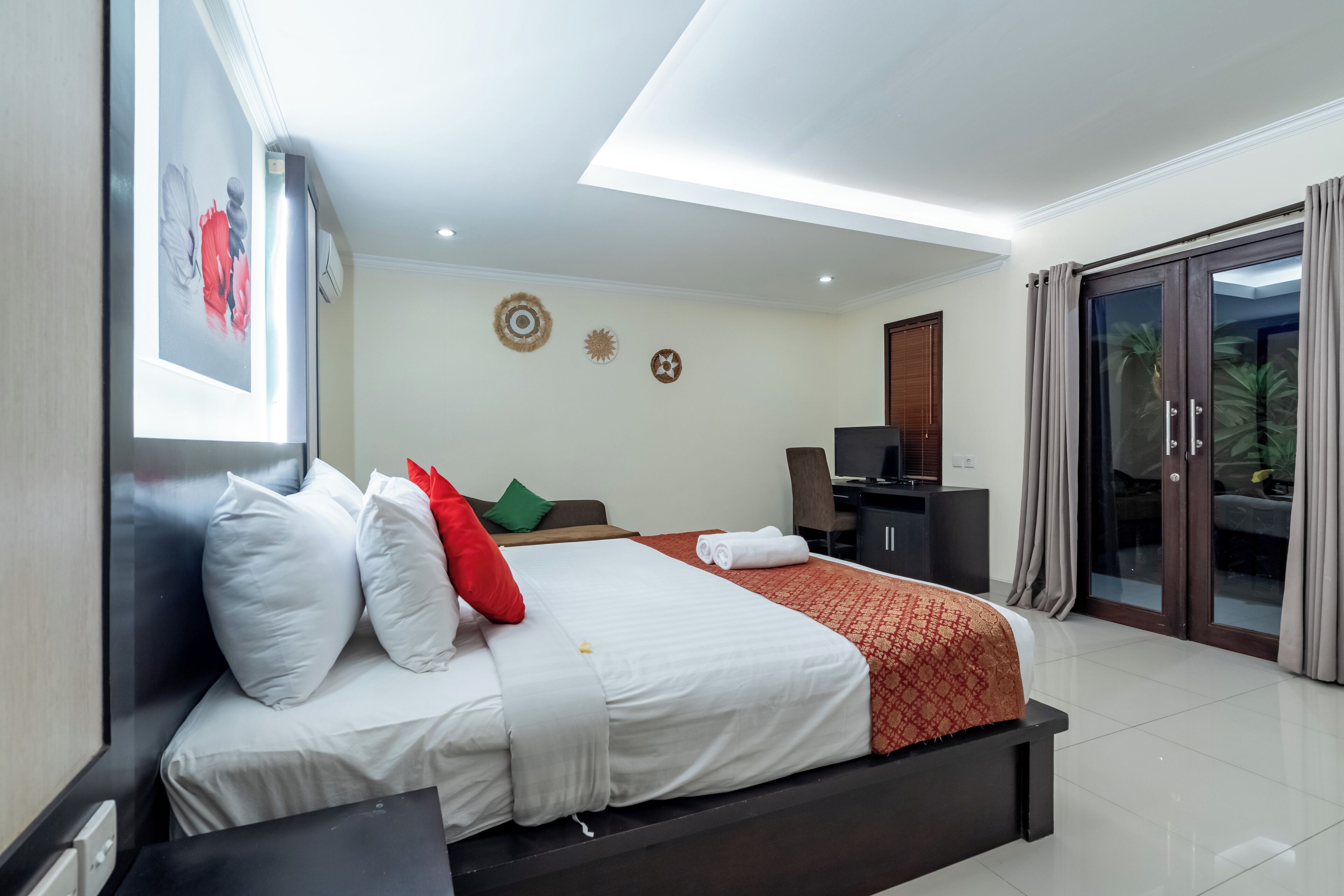 Quarto de hotel com uma cama grande, uma mesa de trabalho, uma cadeira e uma porta de vidro deslizante que dá para uma área externa.