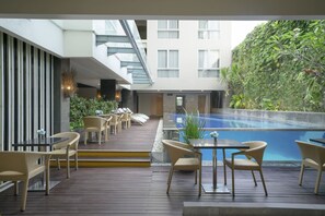 A modern outdoor pool area with wicker furniture and a view of a building with balconies.